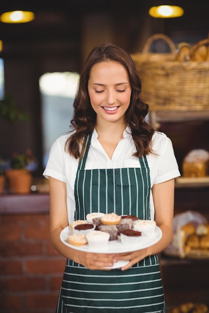 Jolie serveuse montrant une assiette de cupcakes