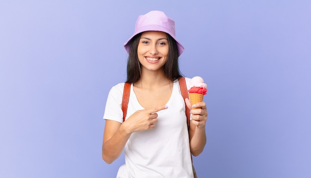 Jolie touriste hispanique à l'air excité et surpris pointant sur le côté et tenant une glace