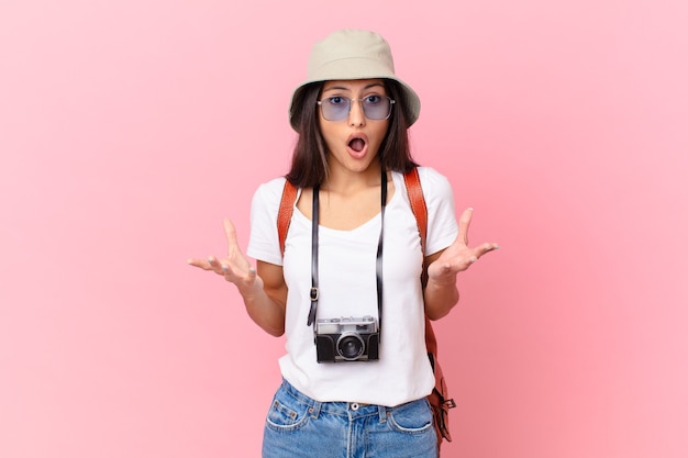 Jolie touriste hispanique étonnée, choquée et étonnée d'une incroyable surprise avec un appareil photo et un chapeau