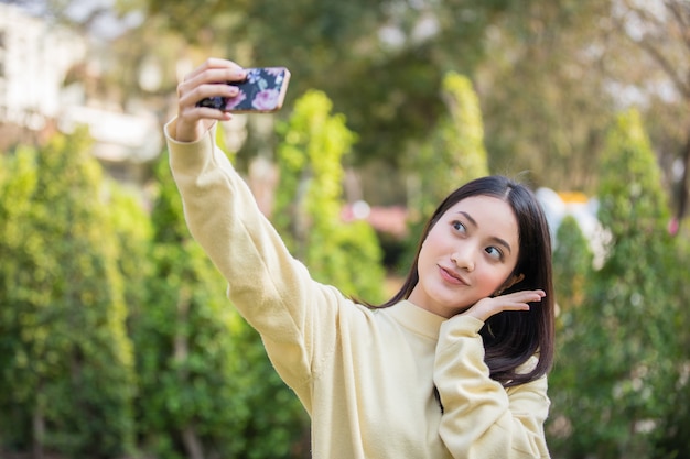 De jolies femmes asiatiques utilisent leurs téléphones pour prendre des selfies et sourire heureux dans le jardin à la maison.