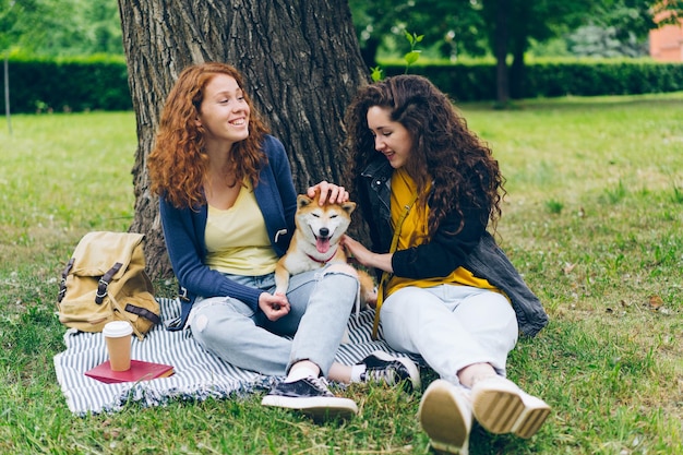 Jolies filles assises sur la pelouse dans le parc avec un chien mignon parlant en s'amusant