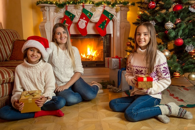 Jolies filles avec une jeune mère assise à la cheminée dans le salon décoré pour Noël