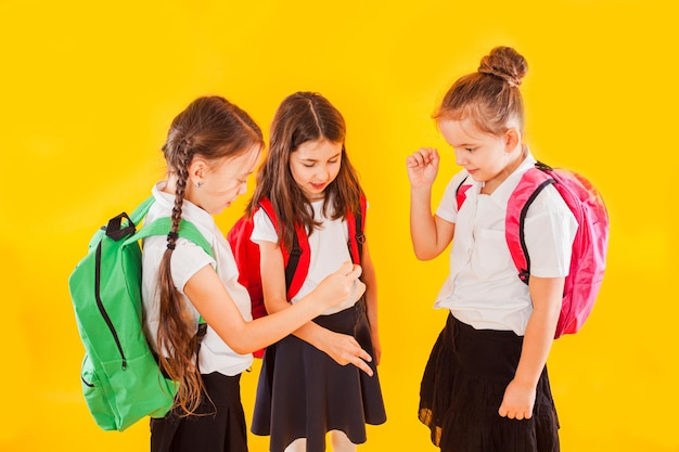 Jolies filles en uniforme avec des sacs à dos sur fond jaune