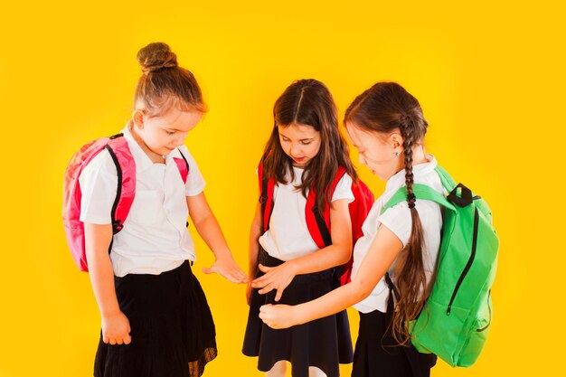 Jolies filles en uniforme avec des sacs à dos sur fond jaune