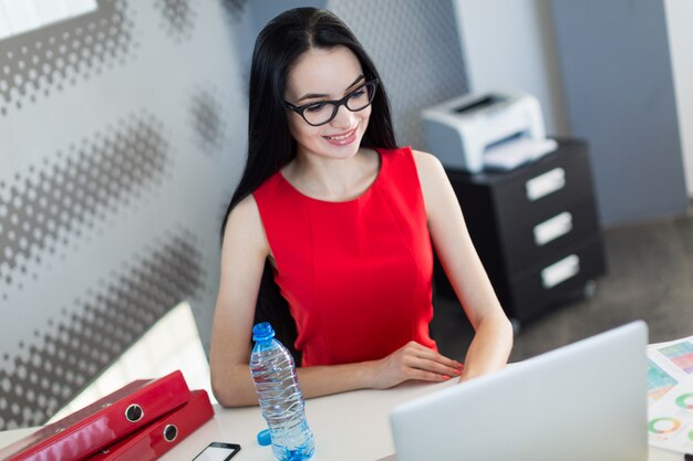 Jolies et jeunes entrepreneurs en robe rouge et lunettes s'assoient à la table et travaillent