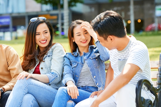 Jolies jeunes femmes riant de la blague de leur ami lorsqu'elles se reposent dehors par beau temps