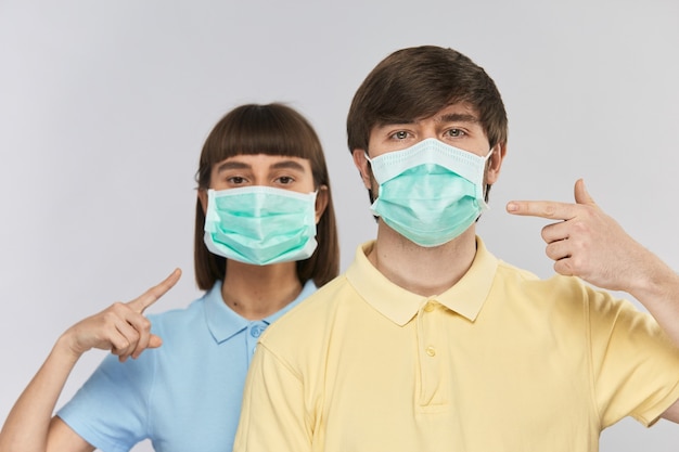 Jolies personnes en masque de protection pointant dessus portant des chemises jaunes et bleues isolées sur bleu, protégez-vous contre la pollution et le coronavirus, copiez l'espace