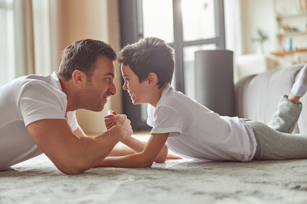 Jolly papa et fils faisant des bras de fer à la maison