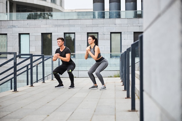 Jolly Slim Femme Et Homme Font Des Squats Pendant L'entraînement Sur L'escalier à L'extérieur Dans Le Centre Urbain