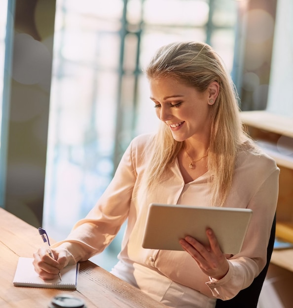 Jongler avec son flux de travail analogique et numérique Photo d'une jeune femme d'affaires souriante travaillant sur une tablette numérique dans un bureau