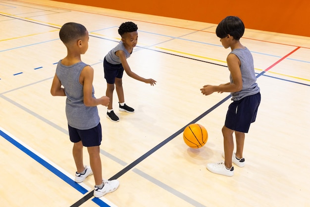 Jouant au basket-ball dans le gymnase de l'école trois garçons s'entraînant au dribbling et au passage