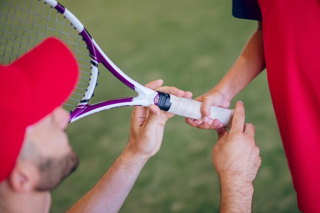 Jouer au tennis. Entraîneur dans un bonnet rouge et un garçon avec une raquette de tennis