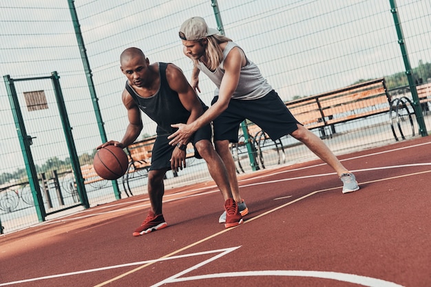 Jouer dur. Deux jeunes hommes en vêtements de sport jouant au basket-ball tout en passant du temps à l'extérieur