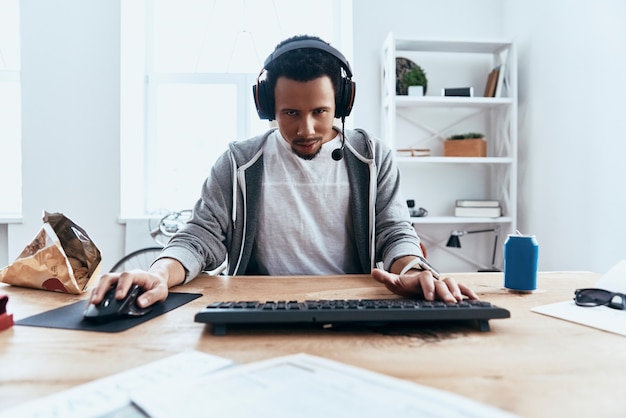 Jouer dur. Jeune homme concentré dans des vêtements décontractés regardant la caméra et souriant tout en jouant à des jeux informatiques à la maison