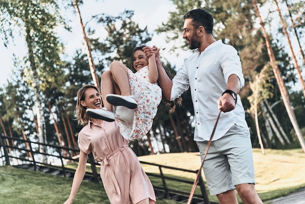 Jouer ensemble. Mère et père balançant sa fille et souriant en marchant dans le parc