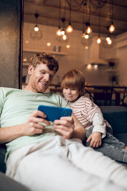 Jouer en ligne. Joli garçon et son père assis ensemble et jouant à des jeux en ligne sur une tablette