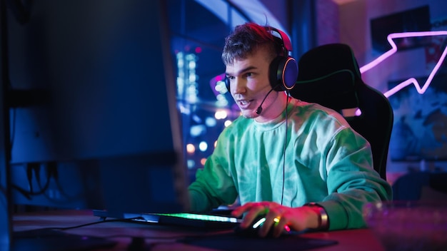 Jouer à la maison Portrait d'un joueur portant des écouteurs et jouant à un jeu en ligne sur un ordinateur personnel Professionnel Joueur masculin élégant profitant d'un tournoi PvP multijoueur en ligne