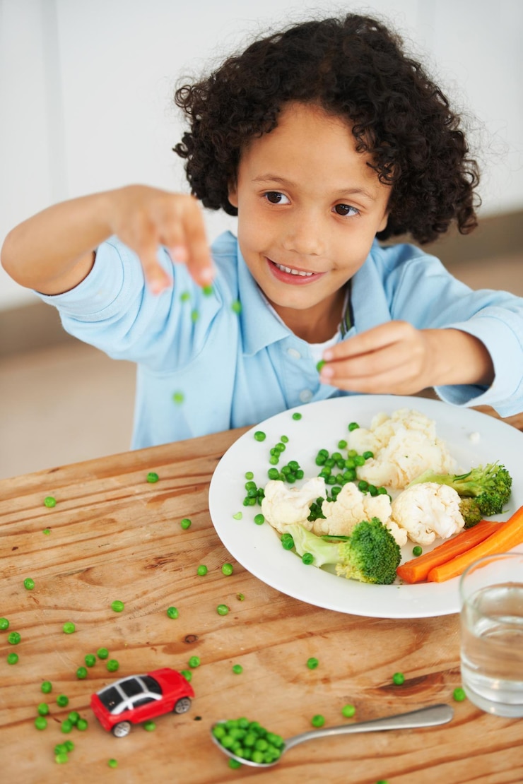 Photo jouer avec votre nourriture un jeune garçon mignon jetant des pois de son assiette partout sur la table