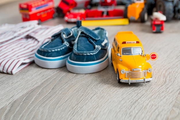 Jouet d'autobus scolaire près de chemises et de chaussures bateau bleues sur une surface en bois grise