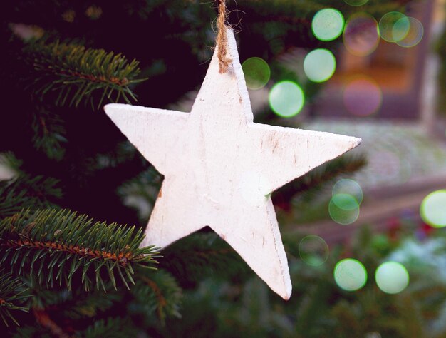 un jouet en bois blanc en forme d'étoile sur un sapin vert dans la rue. Noël