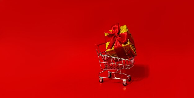 Jouet de caddie avec des cadeaux dans un grand mur rouge de boîte. Copiez l'espace. Réductions, vente. Vente de Noël et du nouvel an.