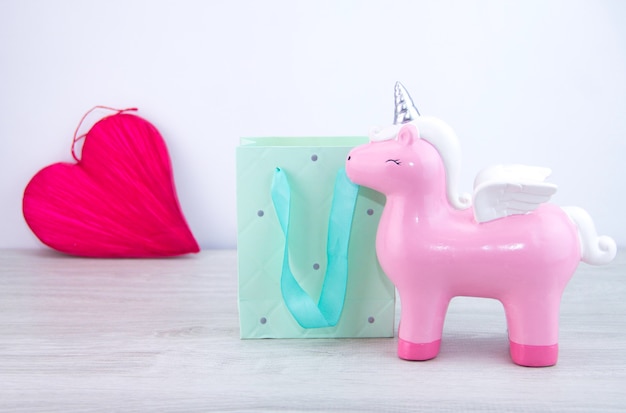 Le jouet licorne rose se tient à côté du sac cadeau. Mise au point sélective. Coeur rouge en arrière-plan. Cadeau à une fille.