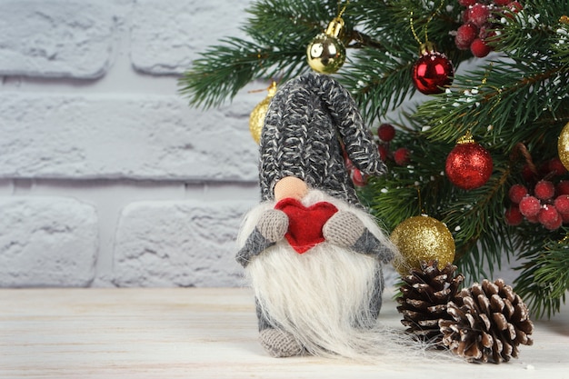 Jouet de nouvel an Père Noël tenir coeur de forme rouge sur fond d'arbre de Noël décoré et mur de briques blanches.