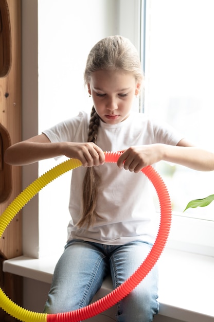 Jouet en plastique anti-stress sensoriel tube pop dans les mains des enfants. une petite fille heureuse joue avec un jouet poptube à la maison. enfants tenant et jouant pop tube couleur jaune et rouge, tendance 2021 année