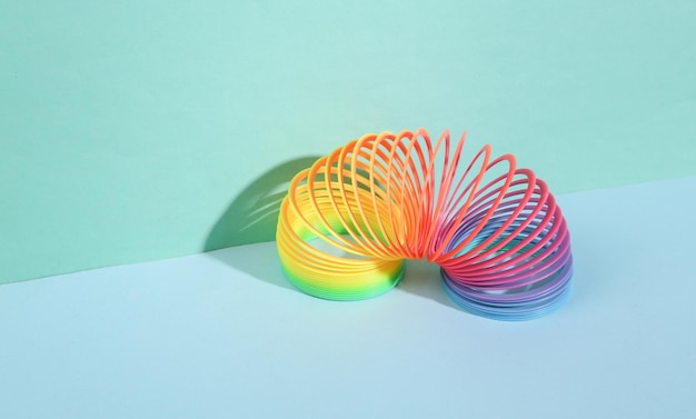 Jouet slinky en spirale multicolore en plastique arc-en-ciel avec des formes géométriques sur fond bleu Minimalisme Nature morte créative