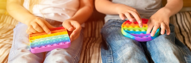 Jouets anti-stress sensoriel pop it dans les mains des enfants. un petit enfant heureux joue avec un simple jouet à fossettes à la maison. les tout-petits tenant et jouant la couleur arc-en-ciel popit, tendance 2021 année. bannière. éclater