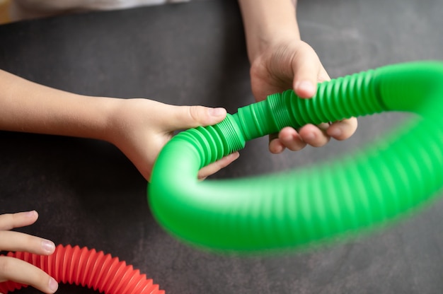 Jouets anti-stress sensoriels à tube pop dans les mains d'un enfant. un petit enfant heureux joue avec un jouet poptube sur une table noire. tout-petits tenant et jouant des tubes pop couleur vive multicolore, tendance 2021 année