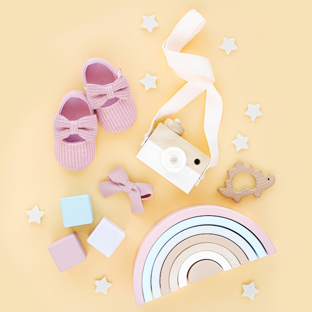 Jouets en bois, chaussons roses et arc-en-ciel pour fille nouveau-née sur fond jaune. Ensemble de trucs et accessoires pour bébé. Mise à plat, vue de dessus