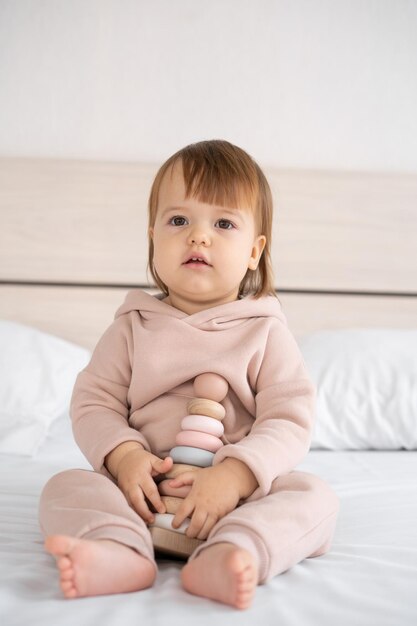 Jouets écologiques pour enfants une petite fille est assise à la maison sur le lit et tient une pyramide colorée en bois moderne avec des anneaux dans ses mains développement de la pensée logique chez les enfants Place pour le texte