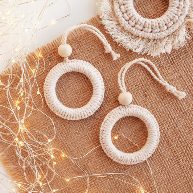 Jouets de macramé de Noël sur papier artisanal Fond blanc Matériaux naturels fil de coton perles de bois et bâton Décorations écologiques ornements décor fait à la main Vacances d'hiver et du Nouvel An