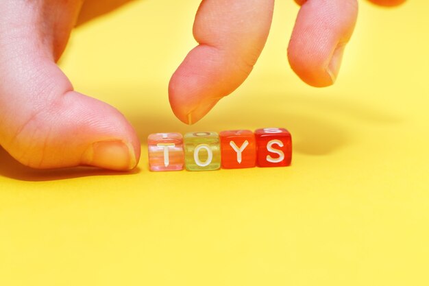 Jouets de mots avec des cubes colorés de perles et la main de l'enfant sur fond jaune