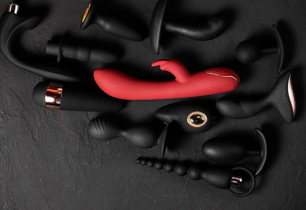 Jouets de plaisir érotiques sur fond noir Gadgets sexuels et appareils de masturbation Gode rose entouré de caoutchouc noir et de jouets sexuels en silicone plugs anaux vibrateurs boules vaginales Vue de dessus