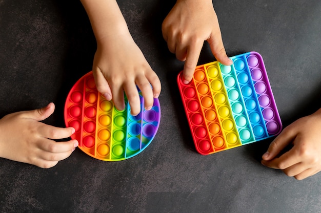Jouets sensoriels anti-stress dans les mains des enfants. un petit enfant heureux joue avec un simple jouet à fossettes sur une table noire.