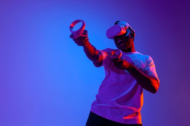 Un joueur afro-américain choqué dans des lunettes de réalité virtuelle tire et vise avec des joysticks