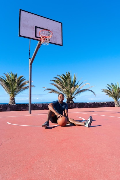 Photo joueur afro de basket-ball sur une aire de sport en plein air assis sur un sol