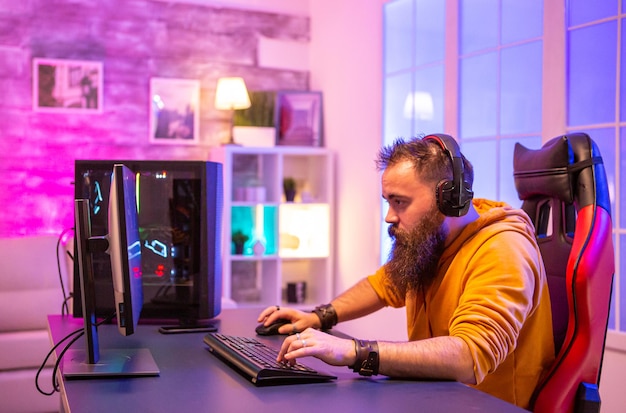 Joueur barbu concentré regardant l'écran du PC dans la chambre avec des couleurs néon