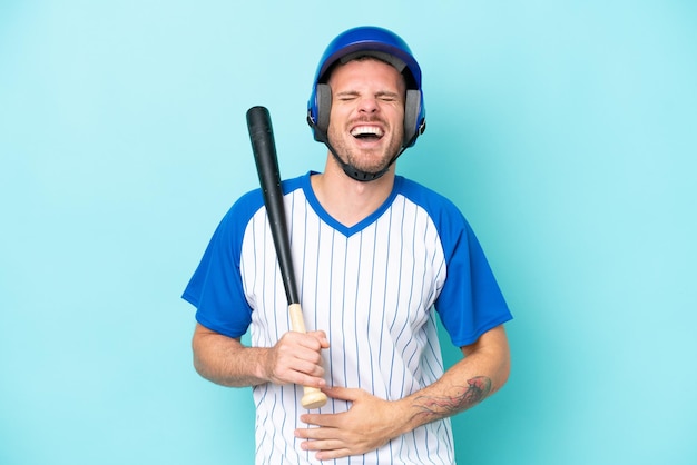 Joueur de baseball avec casque et batte isolé sur fond bleu souriant beaucoup