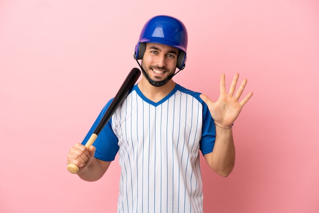 Joueur de baseball avec casque et batte isolé sur fond rose comptant cinq avec les doigts