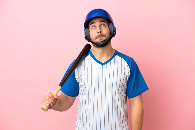 Joueur de baseball avec casque et batte isolé sur fond rose et levant