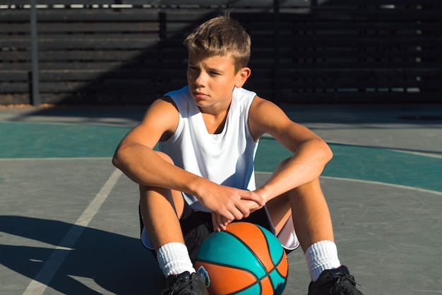 Photo joueur de basket-ball adolescent assis avec ballon sur terrain de sport