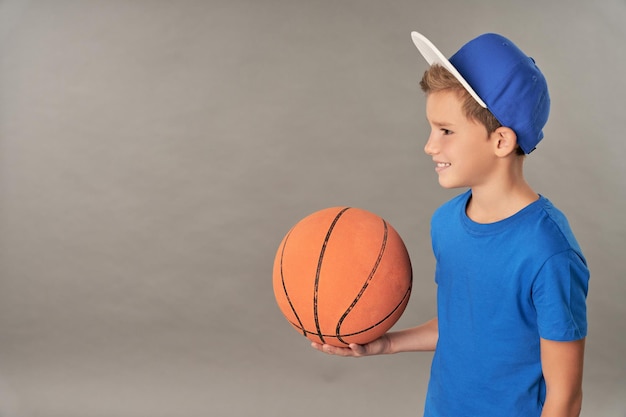 Joueur de basket-ball adorable garçon tenant une balle de jeu orange