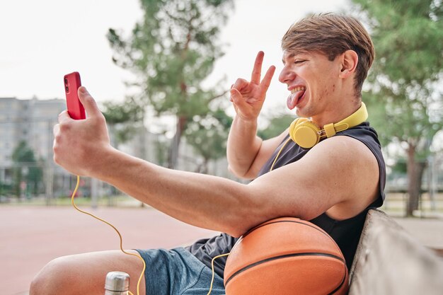 Joueur de basket-ball athlète masculin au repos assis tout en passant un appel vidéo sur son téléphone portable