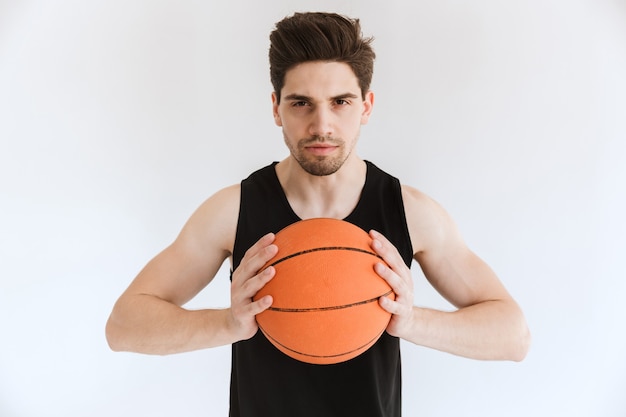 Joueur de basket-ball concentré sérieux jeune homme sportif tenant le ballon isolé.