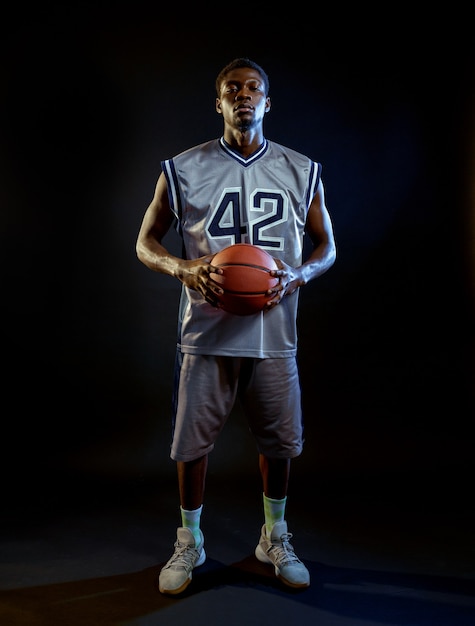 Un joueur de basket-ball concentré tient le ballon. Baller professionnel en vêtements de sport jouant à un jeu de sport, grand sportif