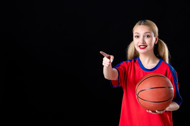 Joueur de basket-ball féminin avec ballon pointant sur quelque chose sur fond noir athlète de jeu