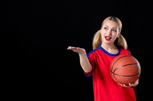 Joueur de basket-ball féminin avec ballon pointant sur quelque chose sur fond noir jouer à l'athlète